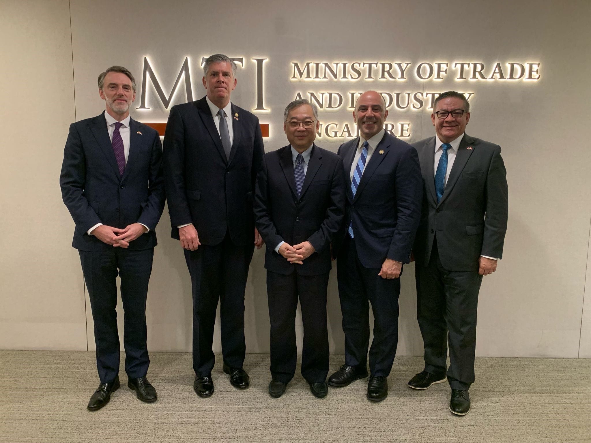 Five men in suits standing in front of a "Ministry of Trade and Industry" sign.